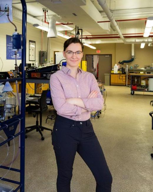 Kettering chemical engineering alum Ashley Switalski stands in a lab next to chemical engineering equipment